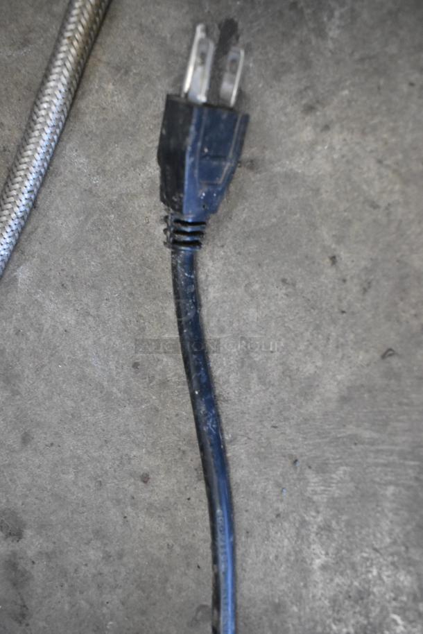Power cord plug of a commercial beverage machine on concrete. 115 volts, 1 phase. Stainless steel construction.
