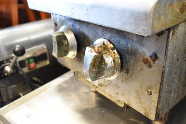 Stainless steel commercial gas-powered 2 burner range, used condition with visible rust and wear on knobs and frame.