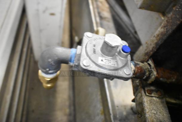 Gas connection detail of a stainless steel commercial countertop gas-powered 2-burner range, showing fittings and rust spots.