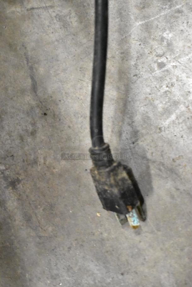 A power cord with a plug, slightly worn, lying on a concrete surface.