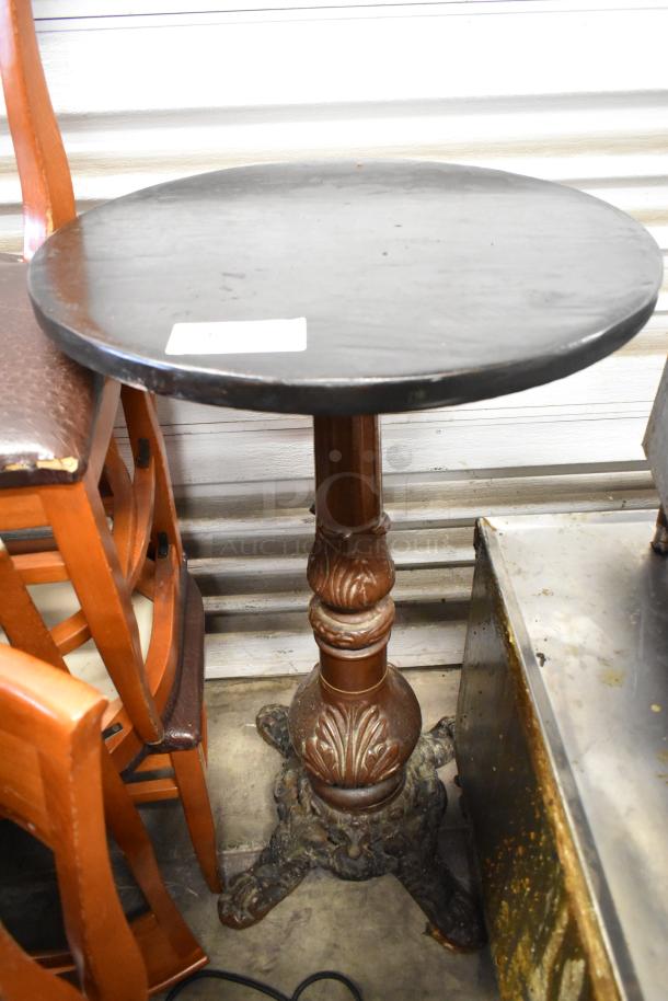 Wooden bar height table with a round tabletop, dark finish, detailed carved pedestal base, some surface wear visible.