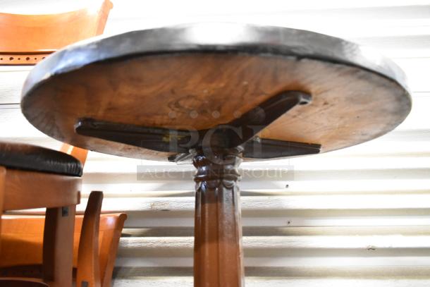 Wooden bar height table with a round tabletop, featuring a sturdy pedestal base. Warm wood tones, slight wear visible.