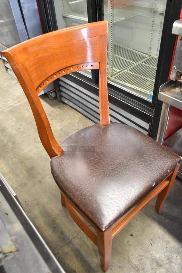 Wooden dining chair with a brown seat cushion. Features a curved backrest with detailed design. Lightly worn condition.