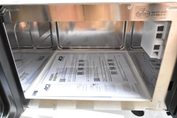 Brand new 2021 Amana RMS10DSA stainless steel commercial microwave with dial controls, documents visible inside.