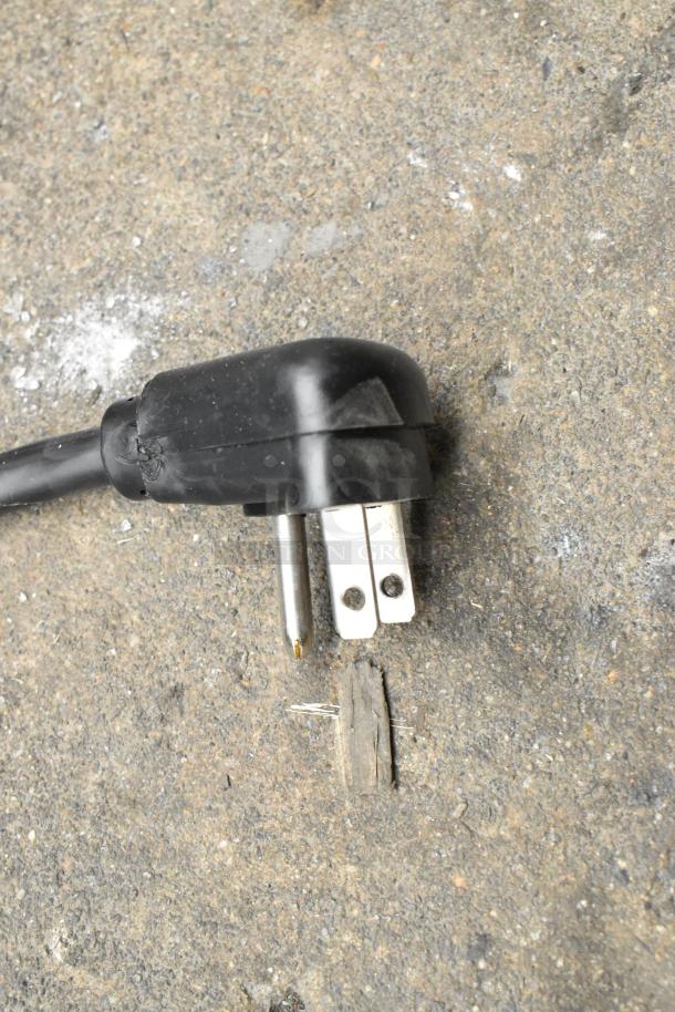The image shows a close-up of a black electrical plug on a rough, textured surface.