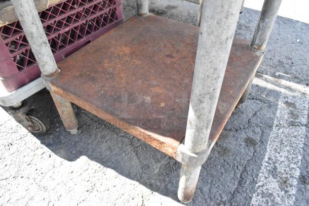 Stainless steel table with a rusted metal under shelf, showing signs of wear. Visible sturdy metal legs on concrete surface.