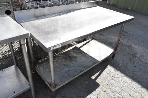 Stainless steel table with backsplash, metal under shelf, and visible label; shows signs of wear. Ideal for kitchens or workshops.