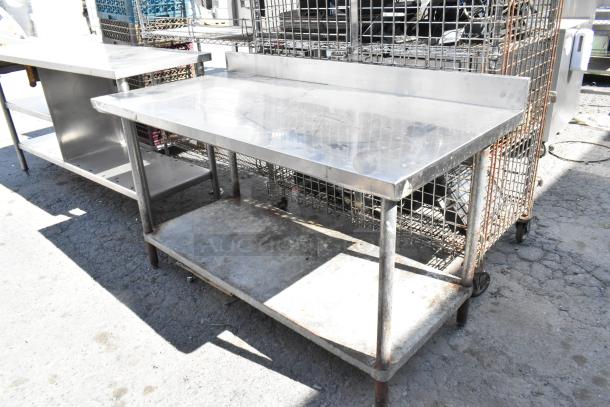 Stainless steel table with back splash and metal under shelf, showing signs of wear, ideal for commercial use.