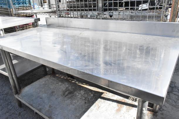 Stainless steel table with backsplash and metal under shelf, showing signs of use and weathering. Ideal for kitchen or workshop.