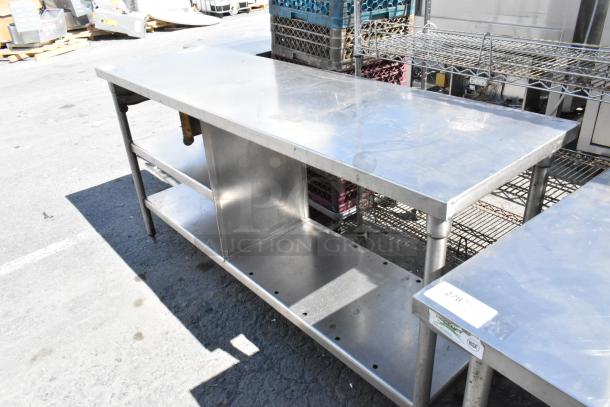 Stainless steel table with a metal undershelf, showing moderate wear; sturdy construction ideal for industrial use.