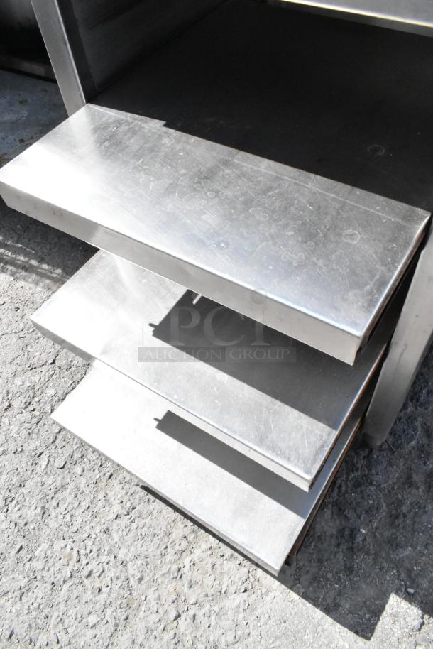 Stainless steel table with under shelves, visible wear, solid construction, ideal for kitchen or workspace organization.