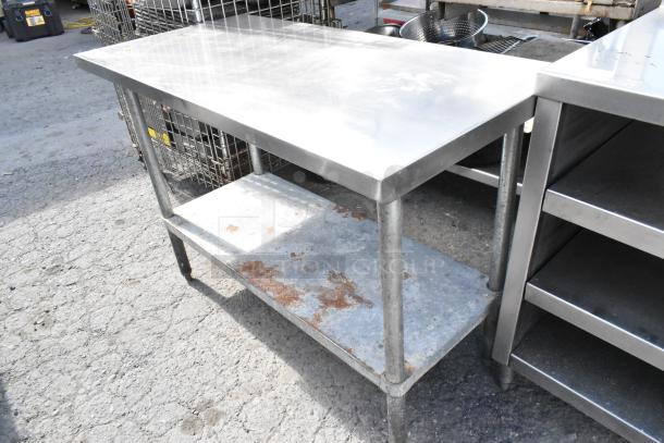 Stainless steel table with metal under shelf, showing signs of rust. Ideal for commercial kitchens. Sturdy and spacious design.