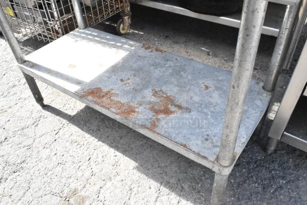 Stainless steel table with metal under shelf, showing wear and rust. Sturdy legs, ideal for industrial use.