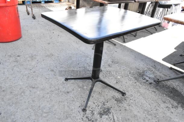 Six black dining height tables with square tops and metal pedestal bases; visible wear on edges.