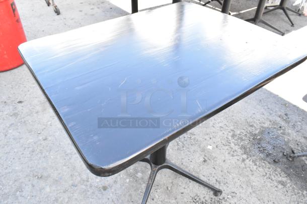 Black dining height table with a smooth top and sturdy metal base, showing minor wear on edges.