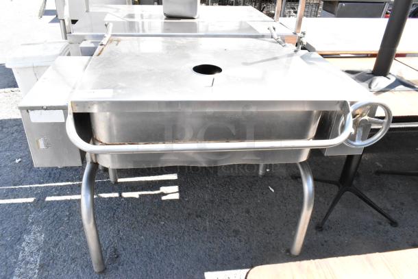 Stainless Steel Commercial Manual Tilt Braising Pan, features a tilting mechanism, sturdy legs, and a front control wheel.