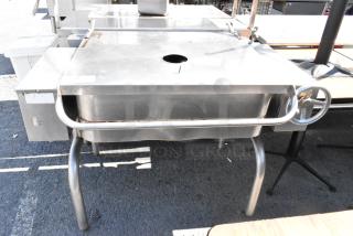 Stainless Steel Commercial Manual Tilt Braising Pan, features a tilting mechanism, sturdy legs, and a front control wheel.