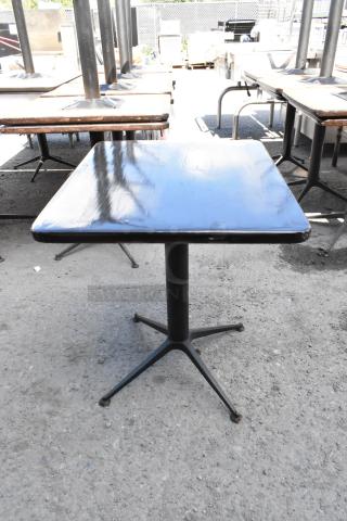 Dining height table with square top and black metal pedestal base. Moderate wear visible. Auction for 9 tables.