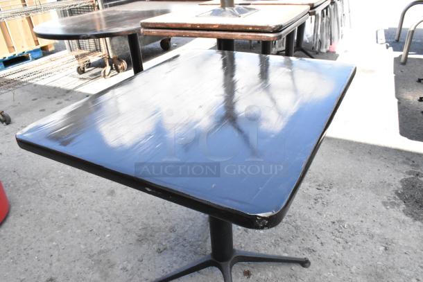 Nine dining height tables, black finish, square and round tops, sturdy bases, some edge wear visible.