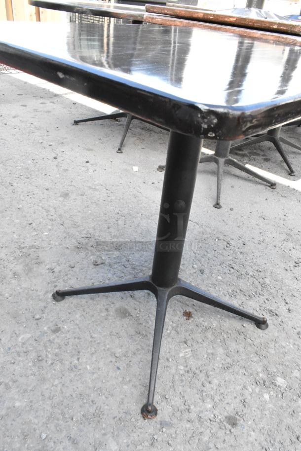 Nine dining height tables with black tops and sturdy metal bases. Used condition with some surface wear.
