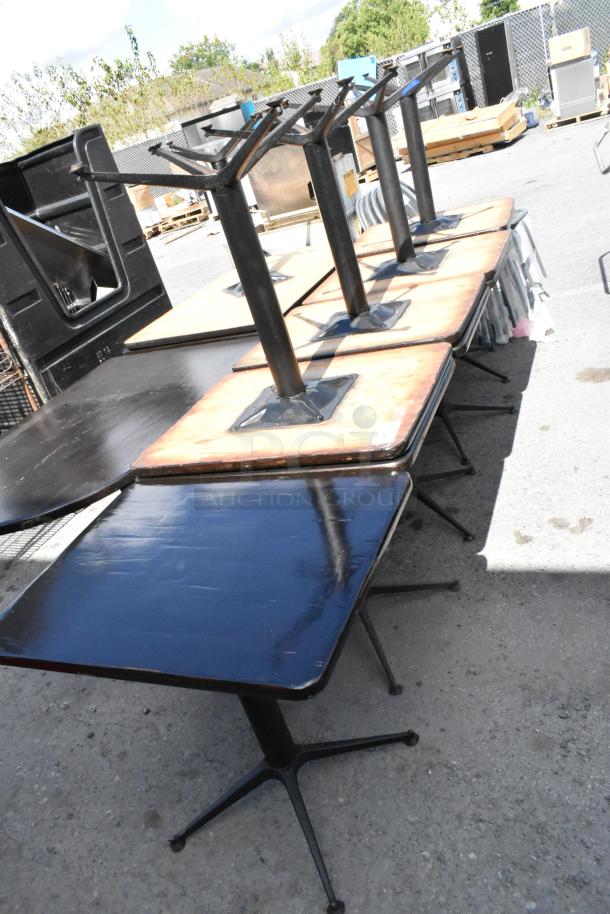 Nine dining-height tables with black bases and dark wood tops, shown outdoors. Signs of wear visible.