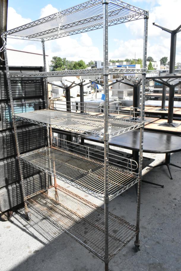 Chrome finish 5-tier wire shelving unit on commercial casters, outdoor setting. Buyer dismantles for shipping.