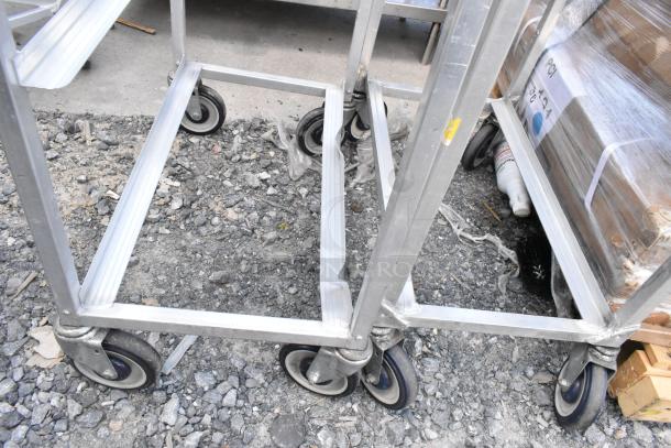 2 metal commercial pan transport racks on heavy-duty casters, suitable for industrial use; shows minor surface wear.