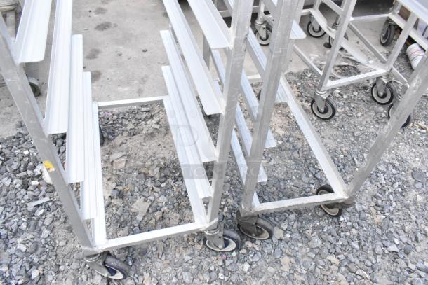 Two metal commercial pan transport racks with casters, one caster missing. Durable design, ideal for kitchen use.