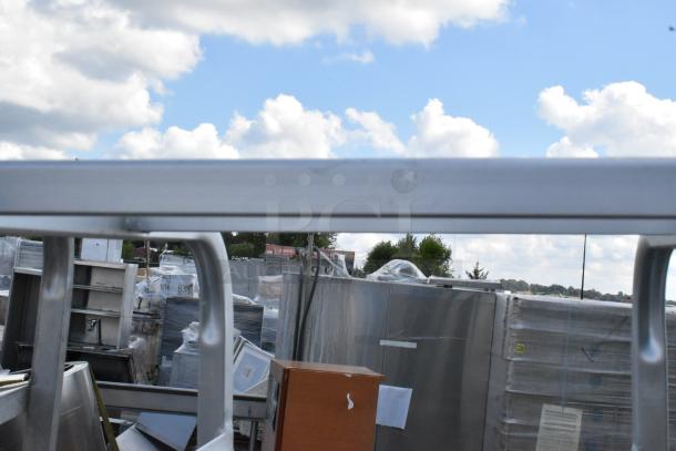 2 metal commercial pan transport racks on casters, one caster missing, used condition, outdoor setting.