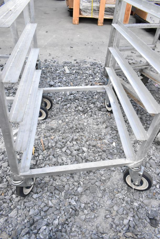 2 metal pan transport racks with commercial casters, sturdy condition, multiple shelves, suitable for kitchen use.