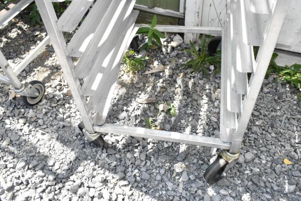 2 metal commercial pan transport racks with sturdy casters, shown on gravel, ideal for kitchen logistics.