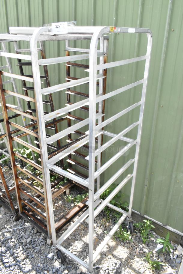 Two metal commercial pan transport racks with multiple shelves and commercial casters, outdoor setting.