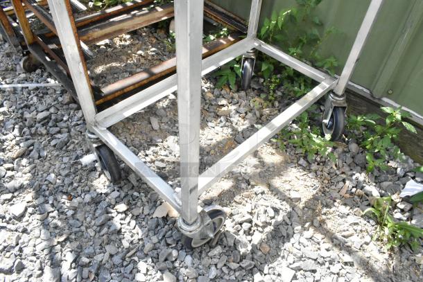 2 metal commercial pan transport rack with sturdy commercial casters, suitable for kitchen use, on gravel surface.