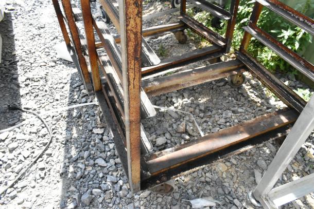 2 metal commercial pan transport racks with oven guides, on casters, visibly rusted, showing signs of wear.