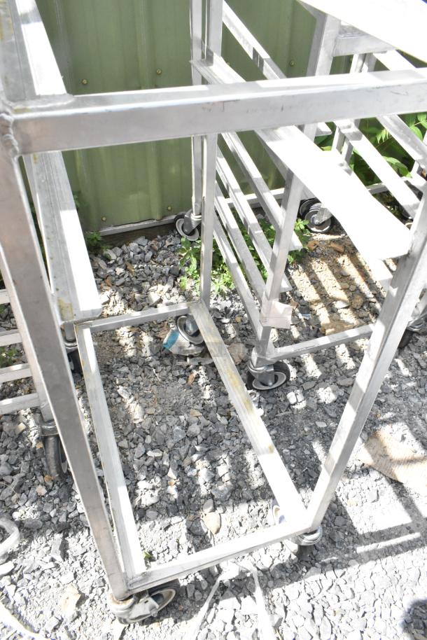 Two metal commercial pan transport racks with commercial casters, shown outdoors. Sturdy frame, used condition.