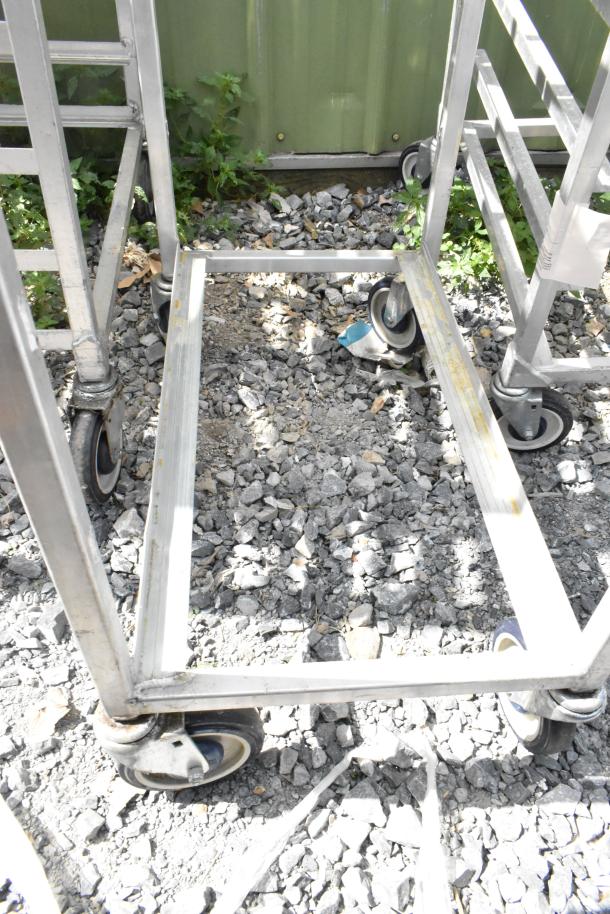 2 metal commercial pan transport racks on casters, sturdy frame, outdoor setting, visible wear, ideal for kitchen use.