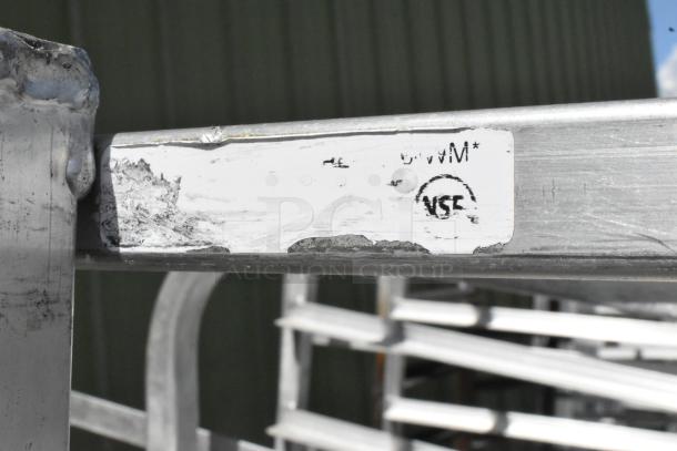 2 metal commercial pan transport racks with casters, showing wear. NSF certification label visible.