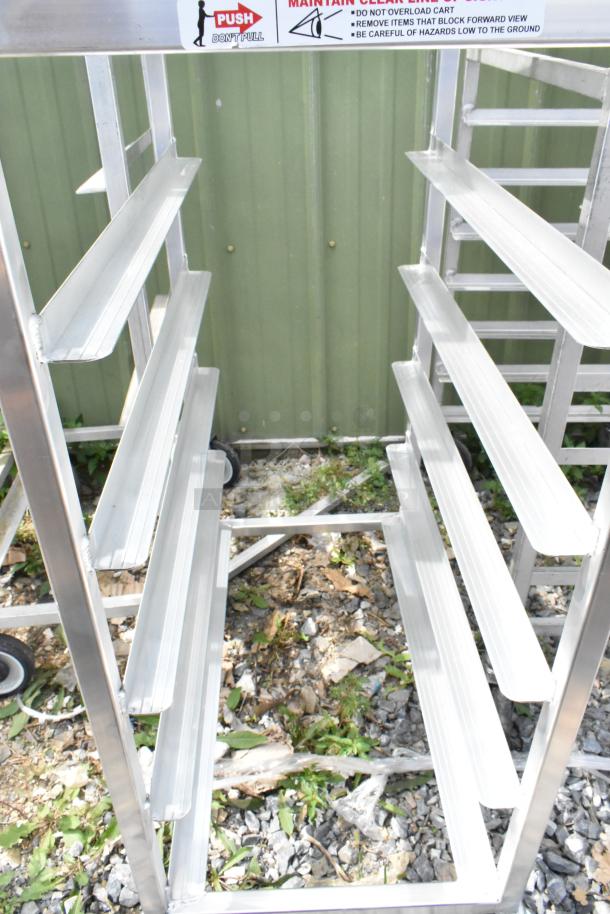 Two metal commercial pan transport racks on casters, with multiple shelves for storage; labeled for safety and handling.