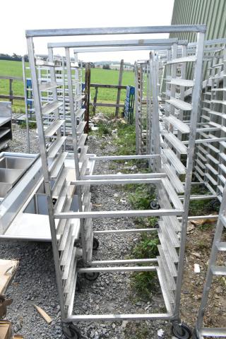 2 metal commercial pan transport racks on casters, outdoor view, multiple shelves, used condition.