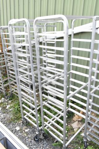 2 metal commercial pan transport racks with multiple shelves on commercial casters, shown outdoors.