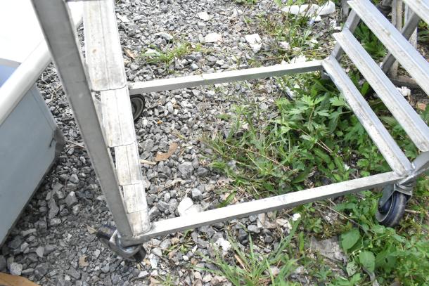 Metal commercial pan transport rack with sturdy construction, commercial casters, and slight wear. Ideal for kitchen use.
