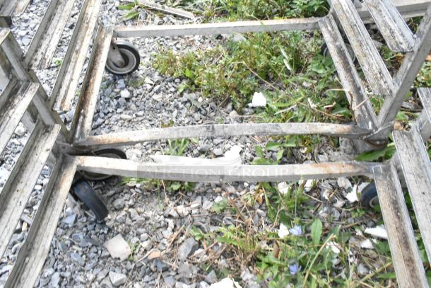 2 metal pan transport racks on commercial casters, slightly weathered, on gravel.