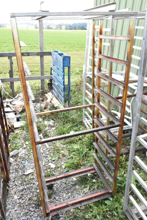 Two metal commercial pan transport racks on casters with an oven guide, showing wear and rust, outdoors.