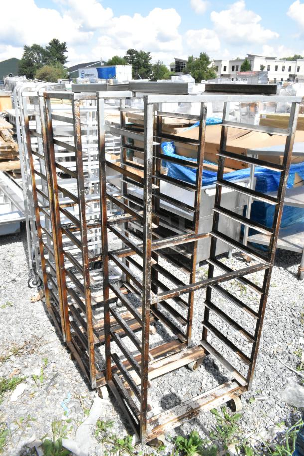 3 metal commercial pan transport racks on casters, with oven guides, displaying visible signs of wear outdoors.