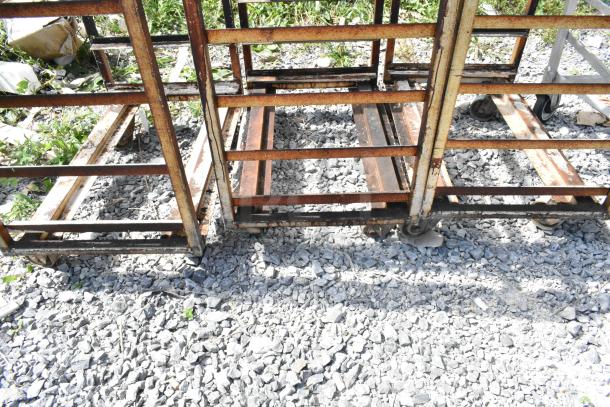 Rusty metal commercial pan transport rack with oven guide and commercial casters, outdoor setting. Multiple racks included.