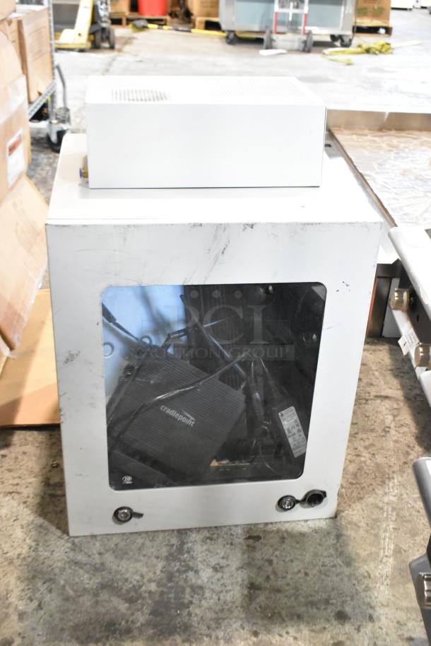 Two metal boxes, one with visible wear and surface marks. A "Cradlepoint" device is seen inside through a clear panel.