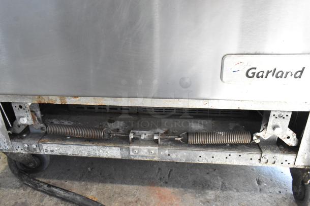 Garland stainless steel 6-burner range with oven, electric, 120/250V, 3 phase, on casters. Visible wear and rust spots.