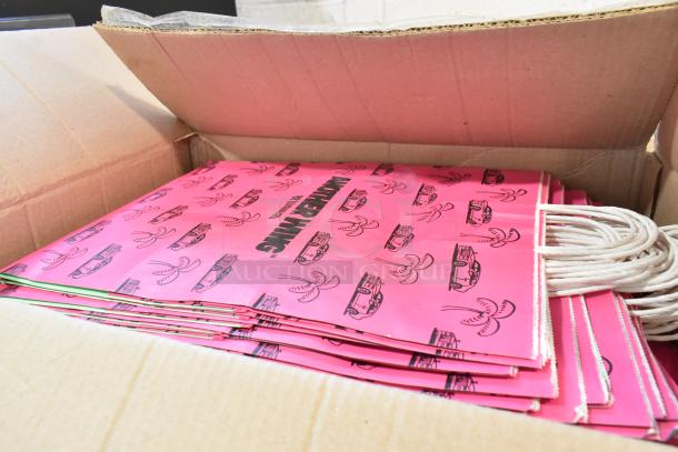 Box of brand new pink paper bags with rope handles, featuring printed car and palm tree design.