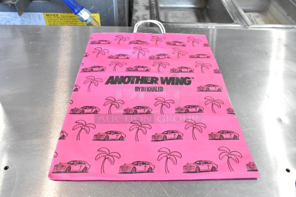 Pink paper bag featuring "Another Wing by DJ Khaled" with palm tree and car graphics, brand new condition.
