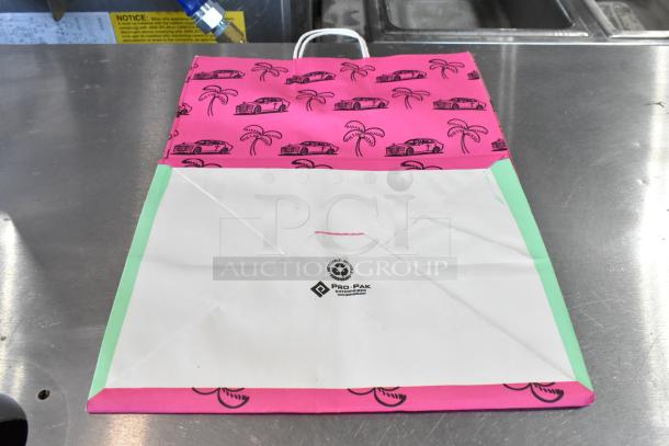 Brand new paper bag from Pro-Pak Enterprises with pink car and palm tree design, and recyclable marking, shown on a metal surface.